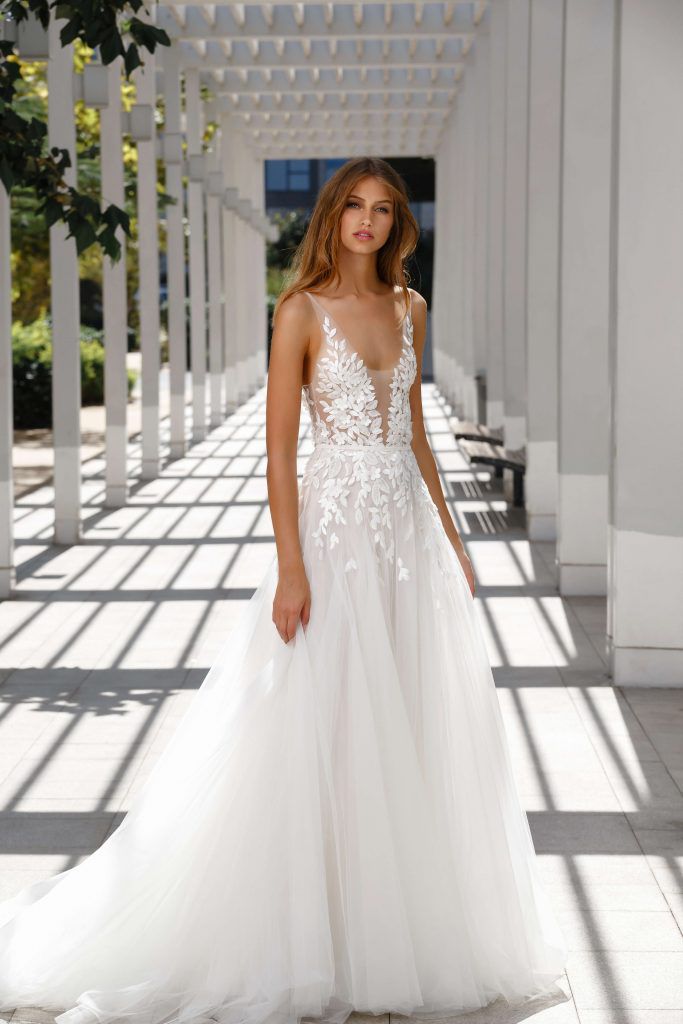 Model in low v-neck silk tulle gown adorned with scattered sparkling leaf appliques and floral accents.