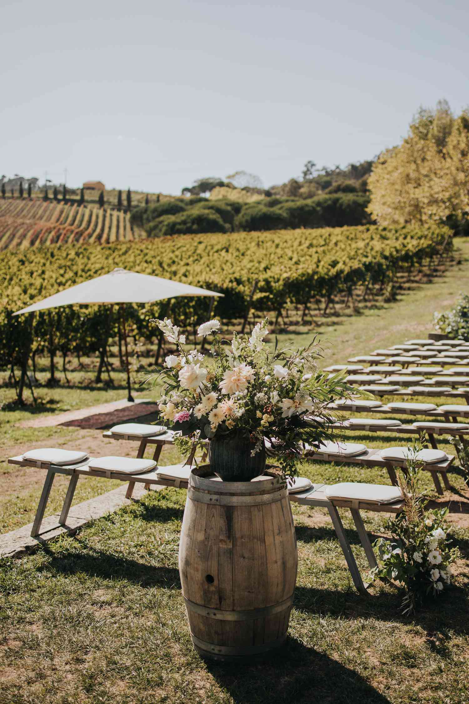 Vineyard wedding ceremony seating with pastel floral arrangements on top of wine barrels
