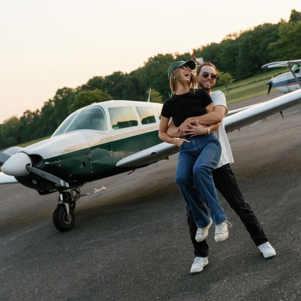 Couple Laughing and Holding Each Other in Front of Vintage Plane on Airfield