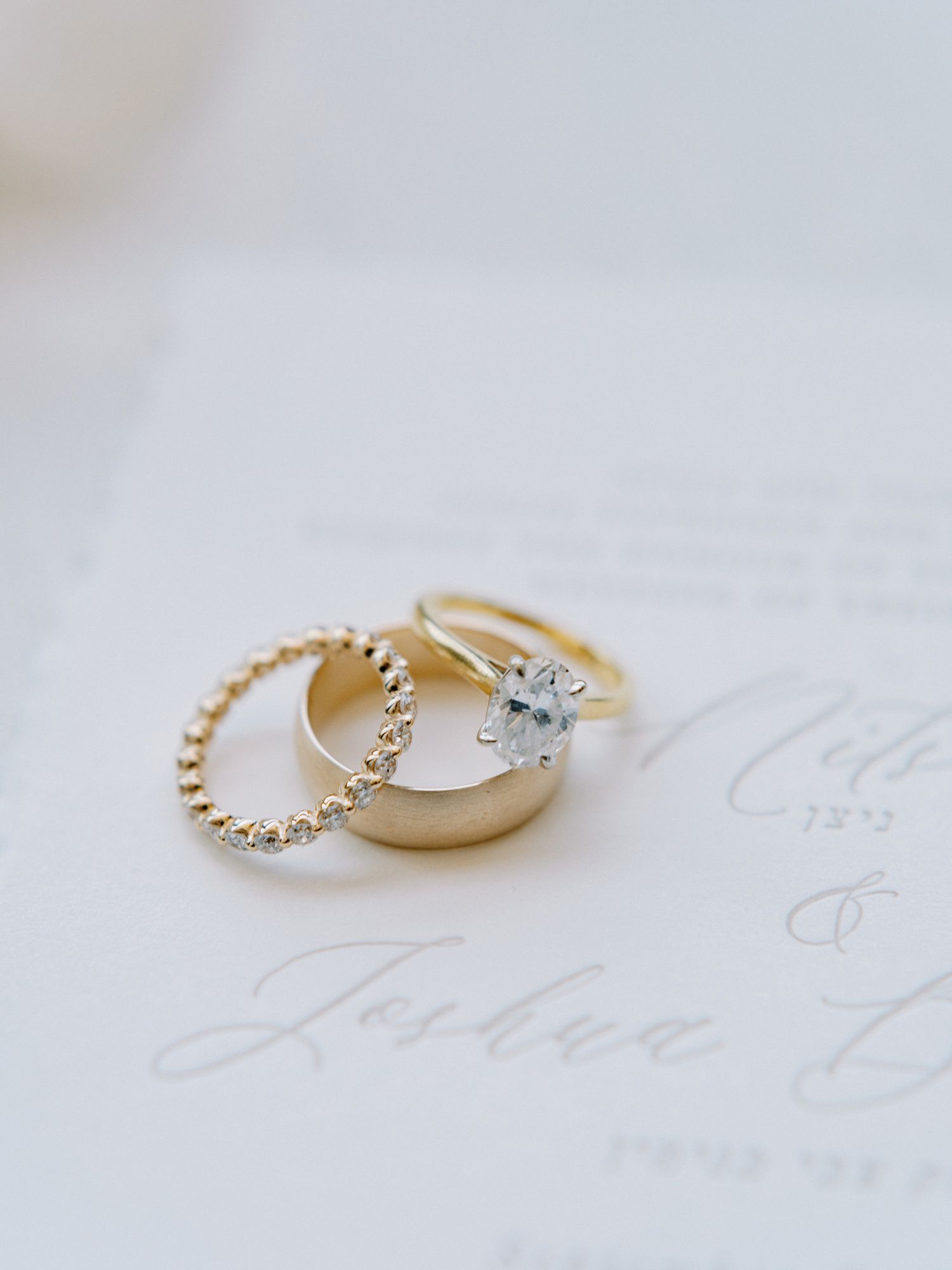 photo of three gold rings sitting on a wedding invitation: an engagement ring and two wedding bands