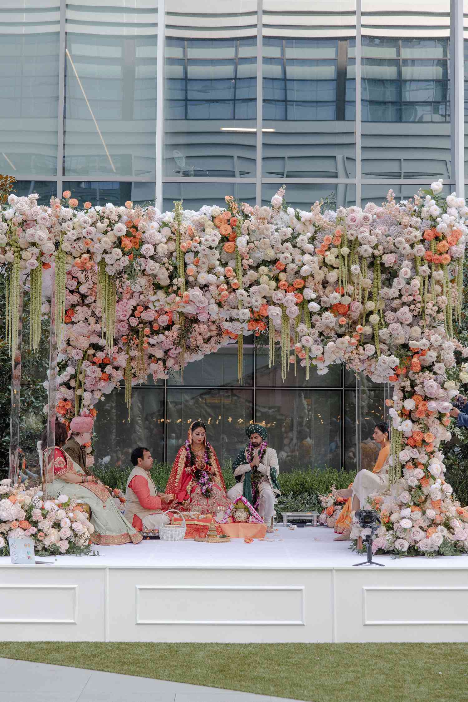 couples praying under a floral mandap with their parents