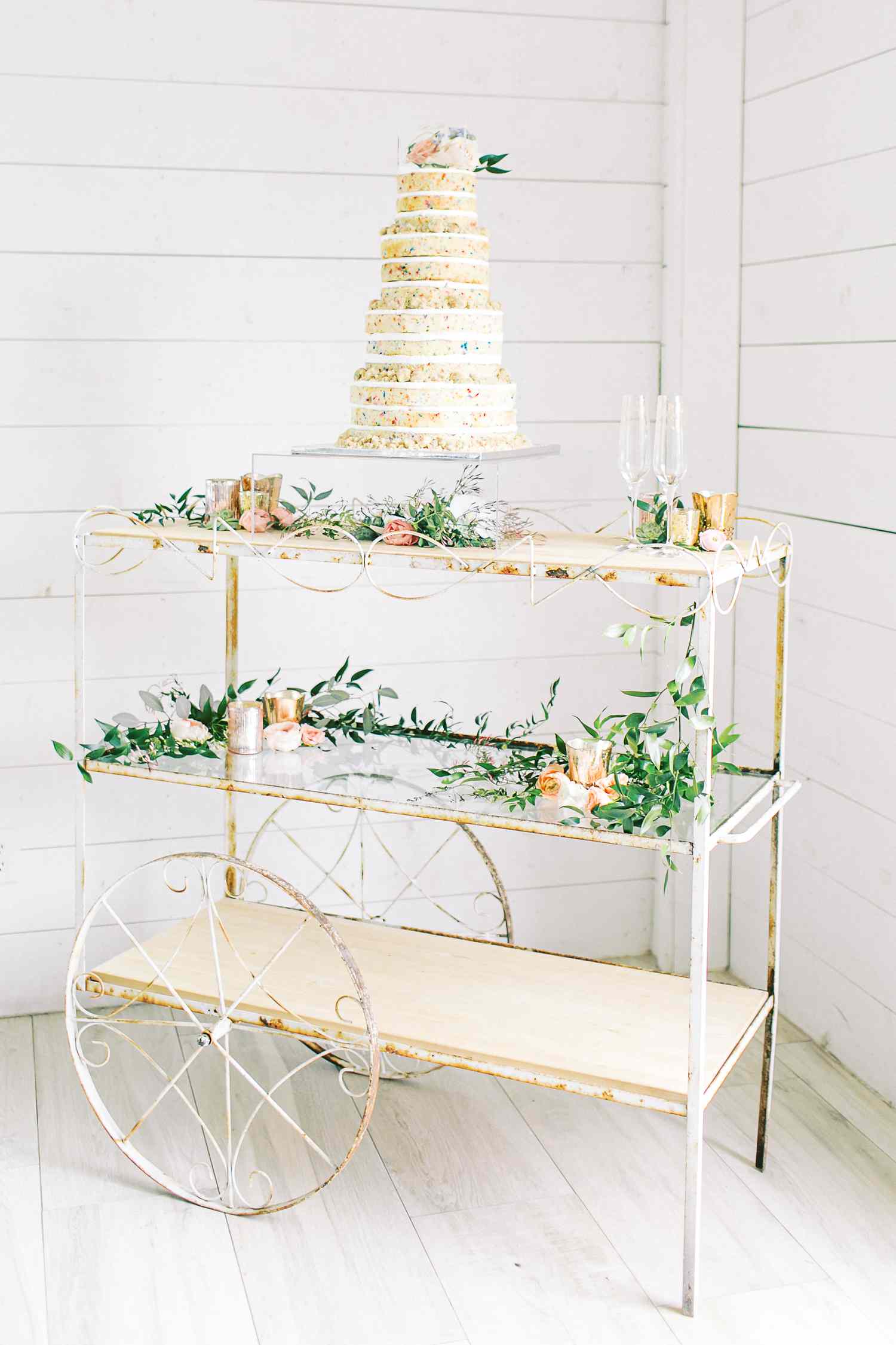 Four-tiered Milk Bar funfetti cake on bar cart with greenery and candles