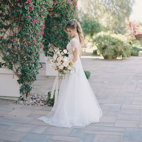 bride looking down at her wedding bouquet while posing amongst a backdrop of vines