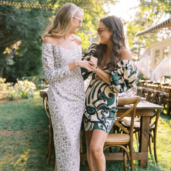 Two people wearing cottagecore wedding guest dresses while standing in front of dinner tables and chairs setup in garden