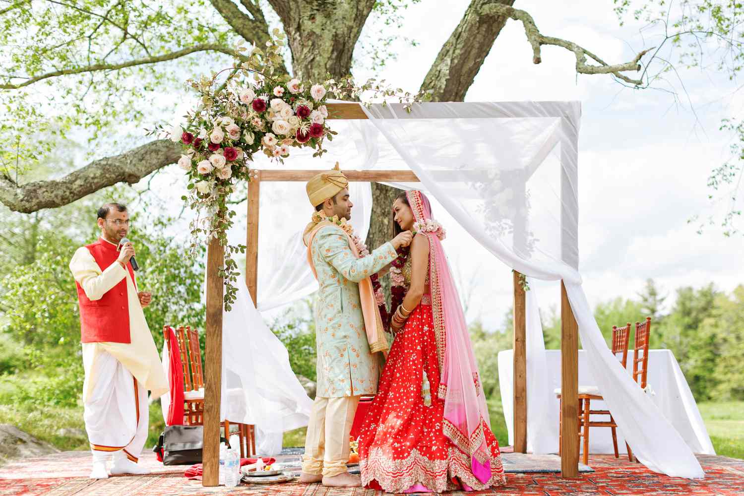 bride and groom under a mandap decorated with roses and a sheer white sheet