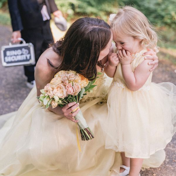 Flower Girl in a Yellow Dress Hugs a Bridesmaid at a Wedding