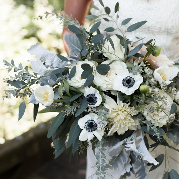 A bride holding a wedding bouquet of white flowers and eucalyptus.