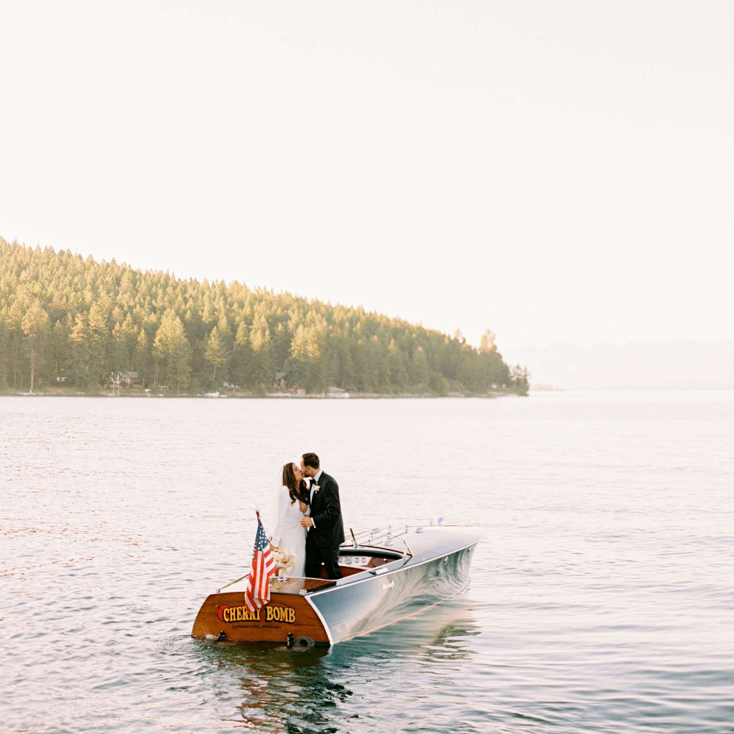 Bride and groom kissing on a boat with with an American flag on a lake