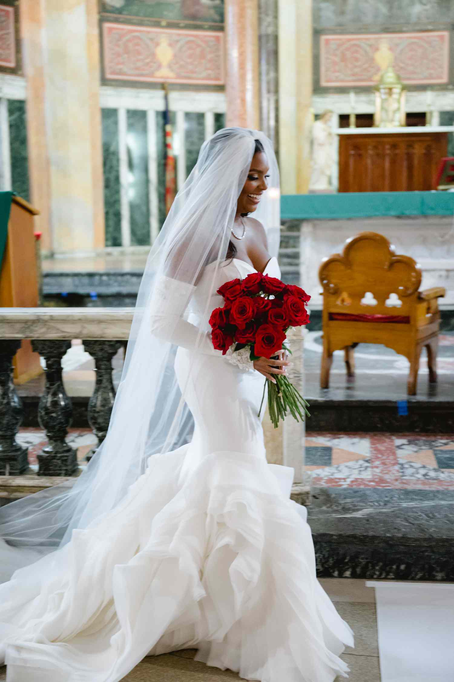 Bride in Strapless Wedding Dress Carrying Red Rose Bouquet in Church