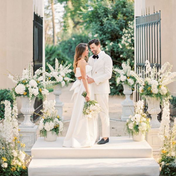 A bride and groom embracing one another while standing on an altar of potted flowers and ferns