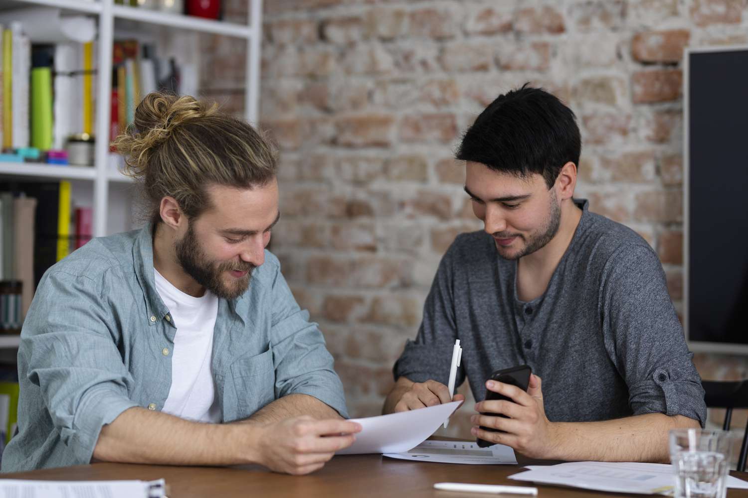 two casually dressed men analyzing reports and documents together at work