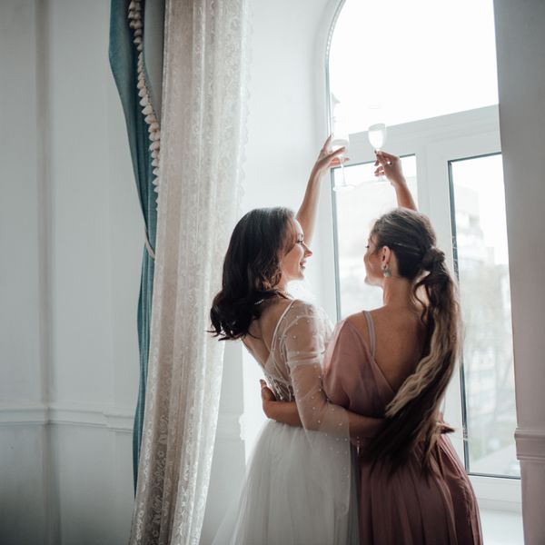 A bride and maid of honor cheers with champagne.