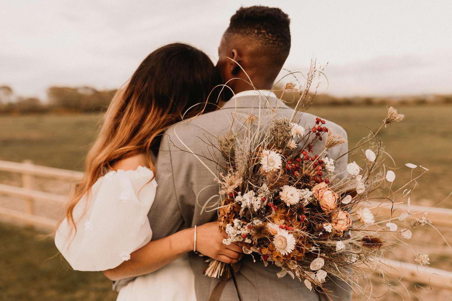 The back of a young couple hugging, showcasing the brides wedding bouquet of dried flowers