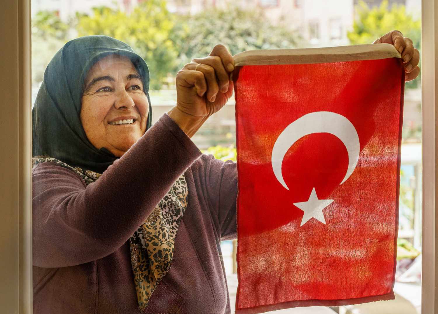 Elder Turkish Woman Hanging Turkish Flag Outside of Window