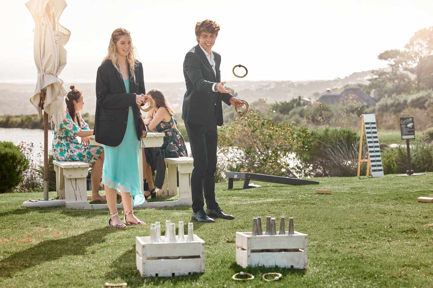 A young woman and man in formal wedding attire playing a ring toss game outside on a lawn during a wedding reception.