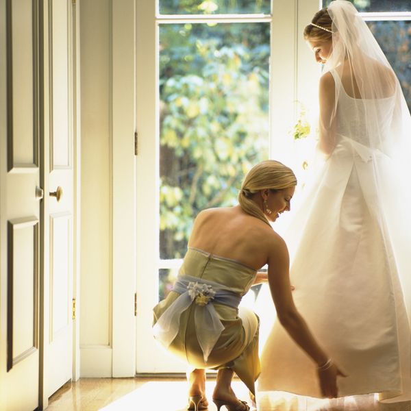 A bride in a white wedding gown and bridesmaid helping fix her train.