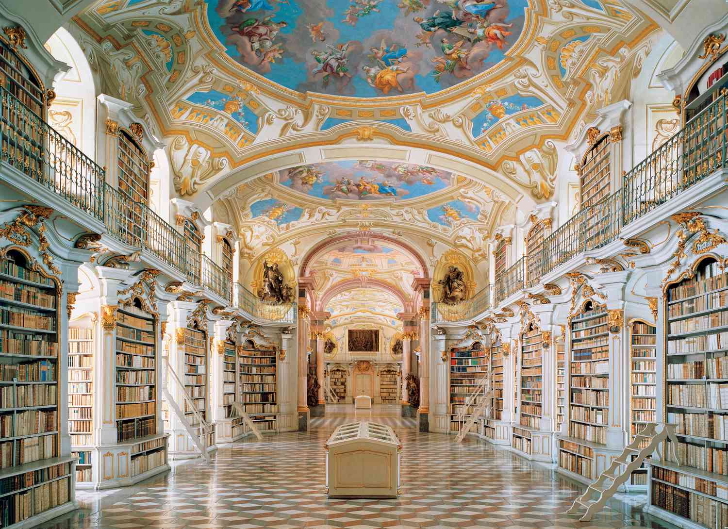 Interior view of Admont Library in Austria, showing ornately-painted ceiling with checkered floor and floor-to-ceiling shelves of books.