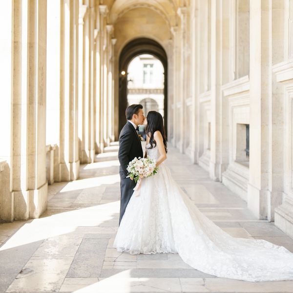 Groom in Black Tuxedo Kissing Bride in Strapless Ball Gown Wedding Dress in Paris Archway Wedding Venue