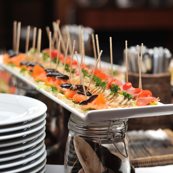 Tray of Appetizers on Skewers That Rests on Mason Jars Beside Stack of Plates
