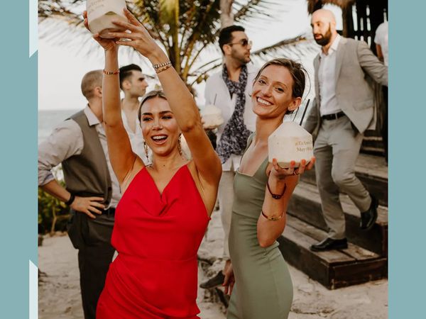 Two wedding guests in cocktail dresses holding coconut beverages