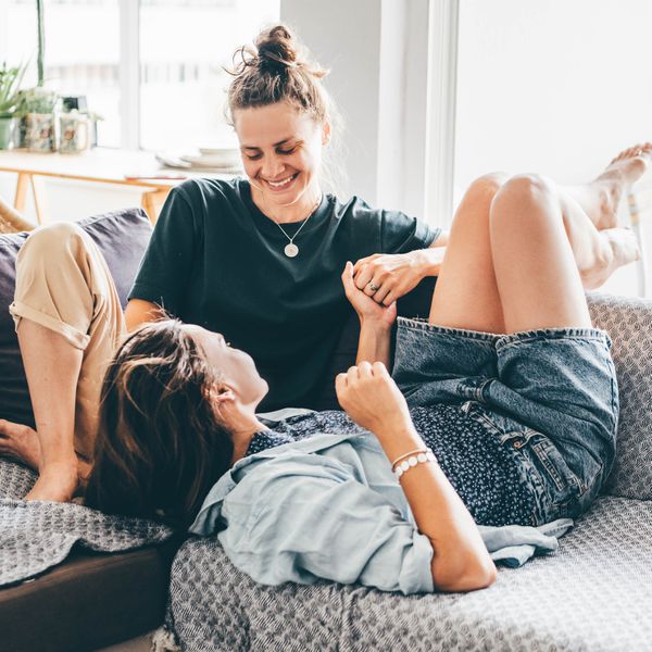 Two women in a relationship smiling and laughing while talking on the couch at home and holding hands.