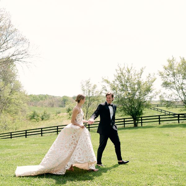 Bride in Strapless Wedding Dress with Low Bun Holding Hands with Groom in Black Tuxedo Walking Outside