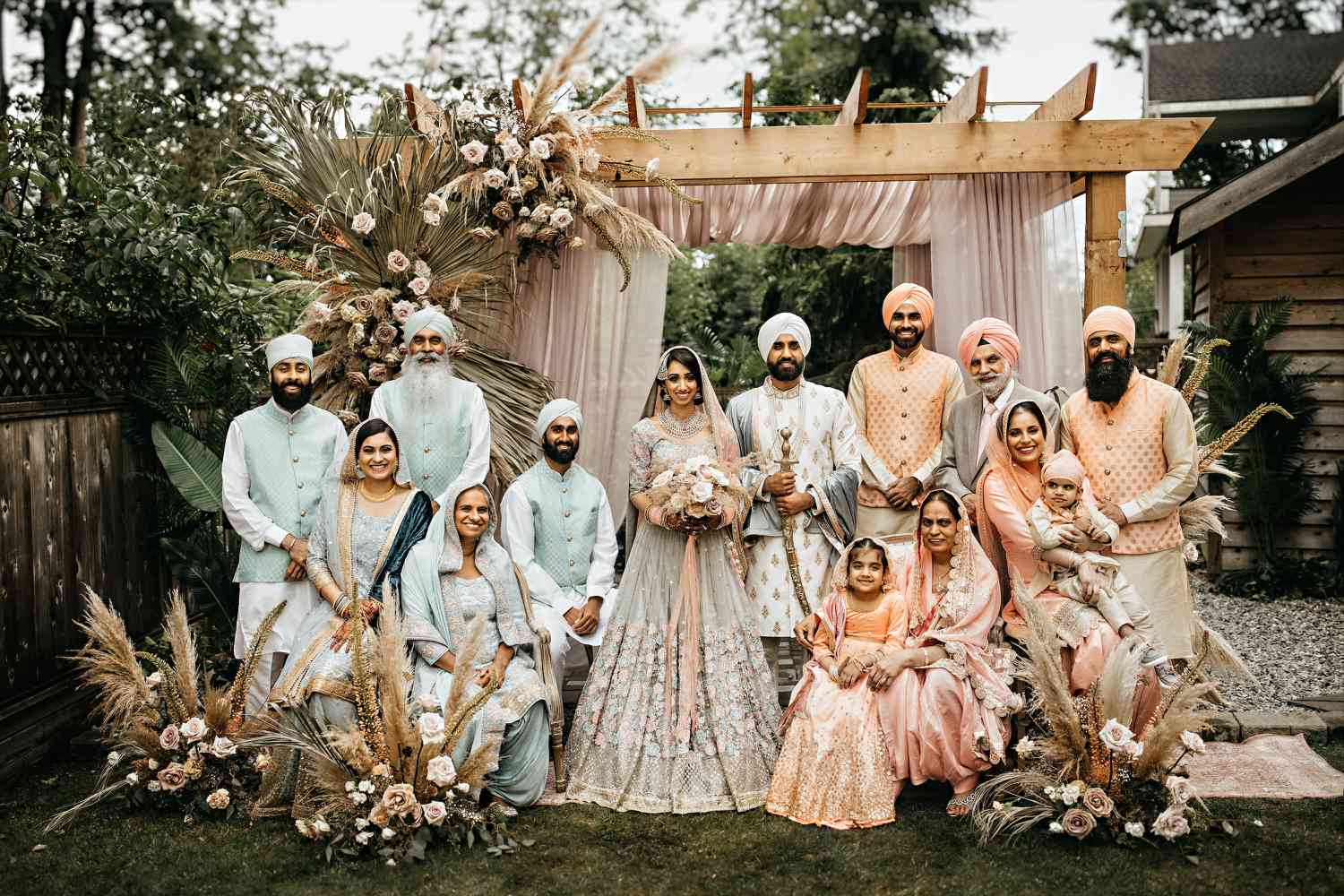 Sikh bride and groom posing with their family during an outside wedding reception