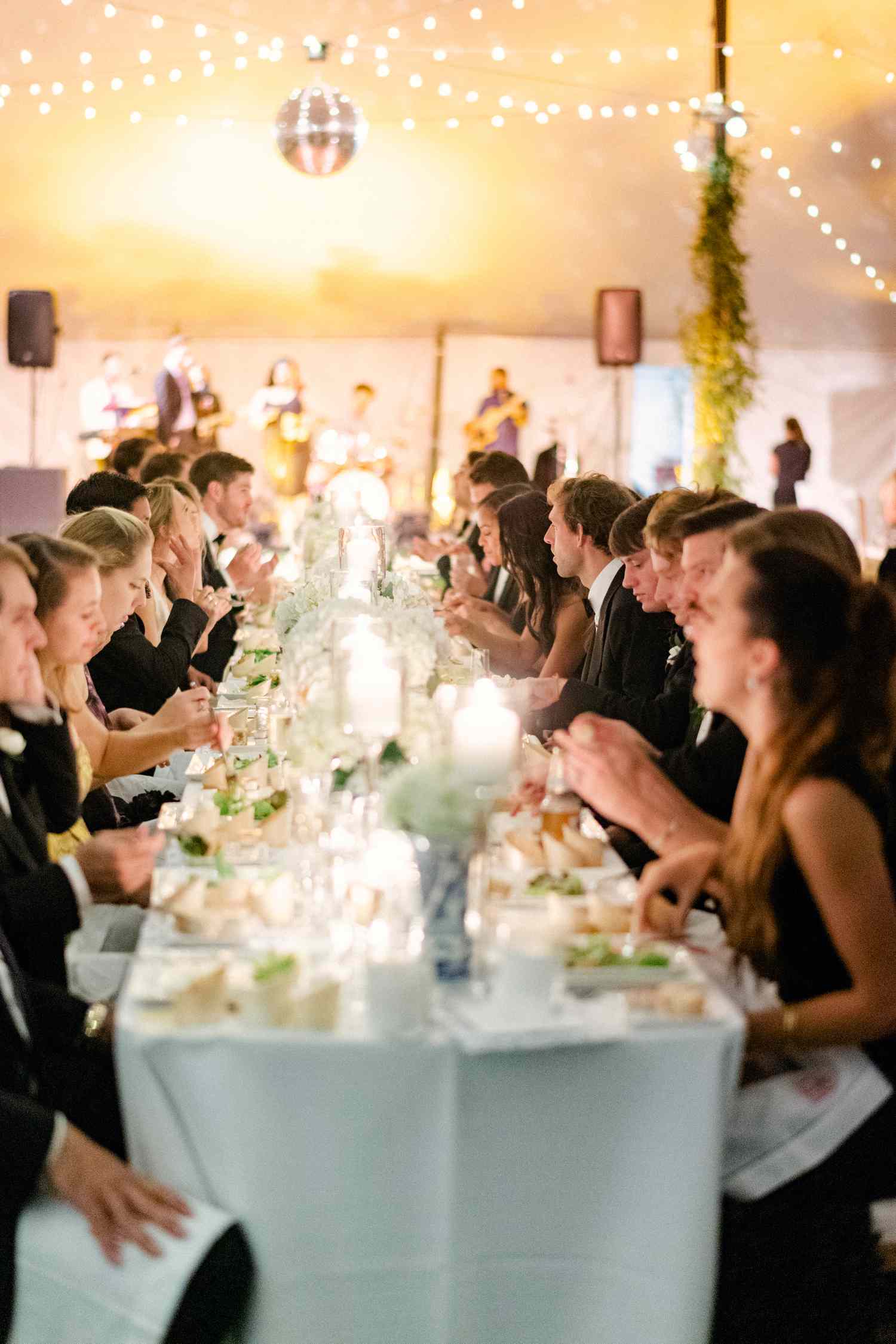 Bride and Groom and Their Wedding Party Sit and Eat Dinner at the Head Table at Their Wedding Reception