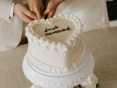 Heart-Shaped Lambeth Wedding Cake on White Stand With Couple Cutting Into It 