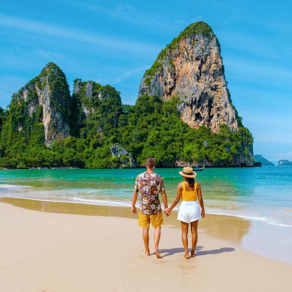 Man and Woman Holding Hands on the Beach While Facing Rock Structure in the Ocean