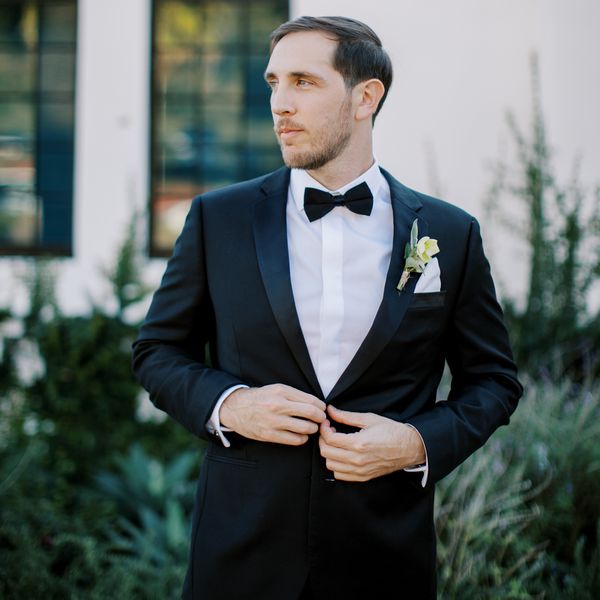 groom looking away wearing a black tuxedo and single flower boutonnière