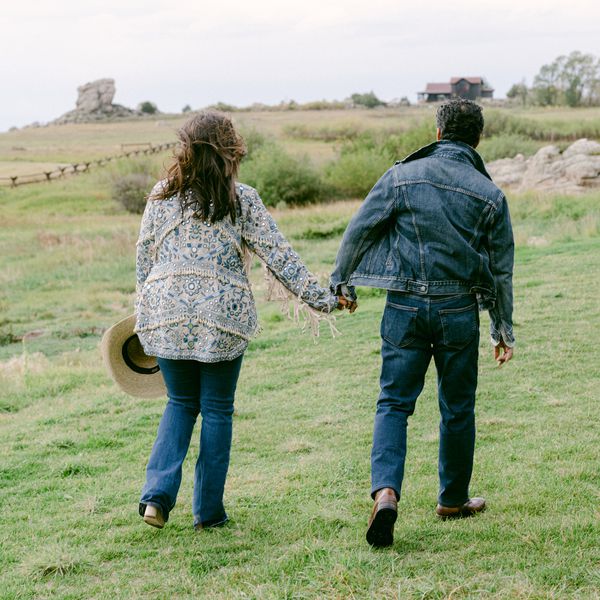 man and woman holding hands in an open field wearing denim