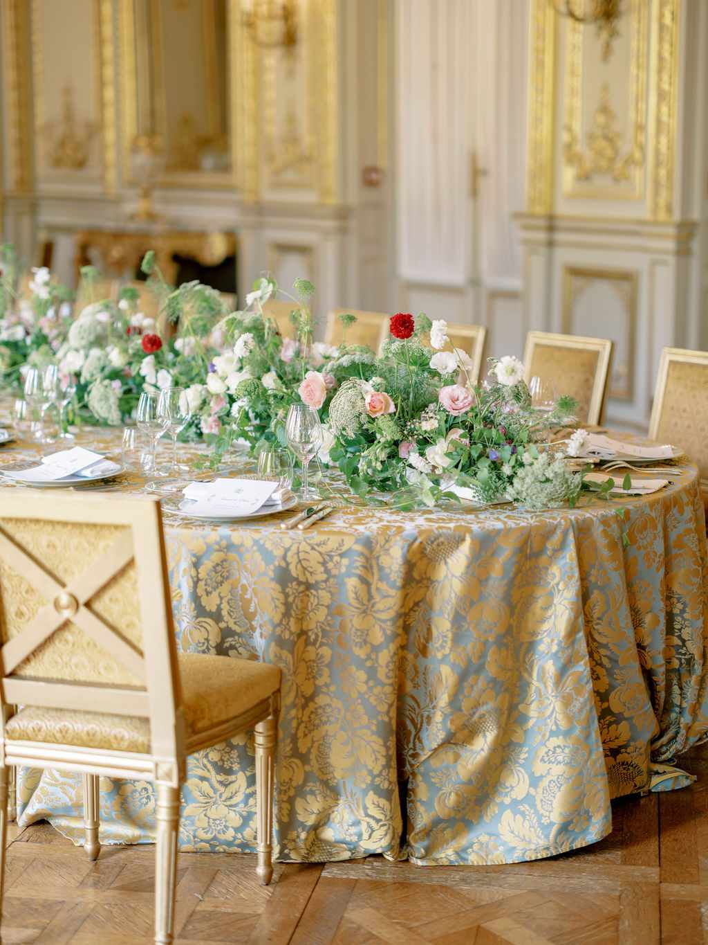 blue and gold paisley tablecloth on a long oval reception table at opulent dinner wedding reception with low floral centerpieces with greenery and roses