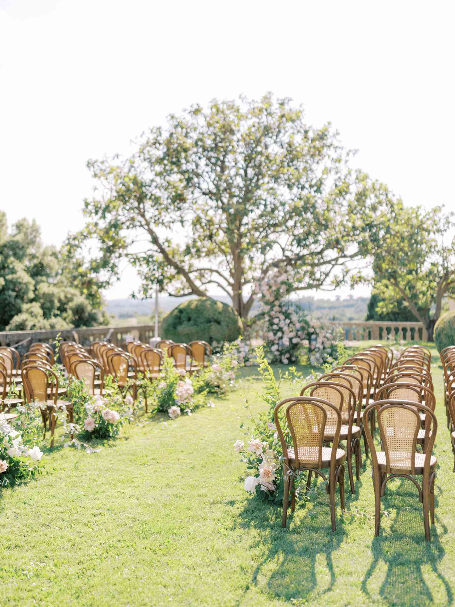 A wedding aisle with green grass, pink flowers, and wooden chairs