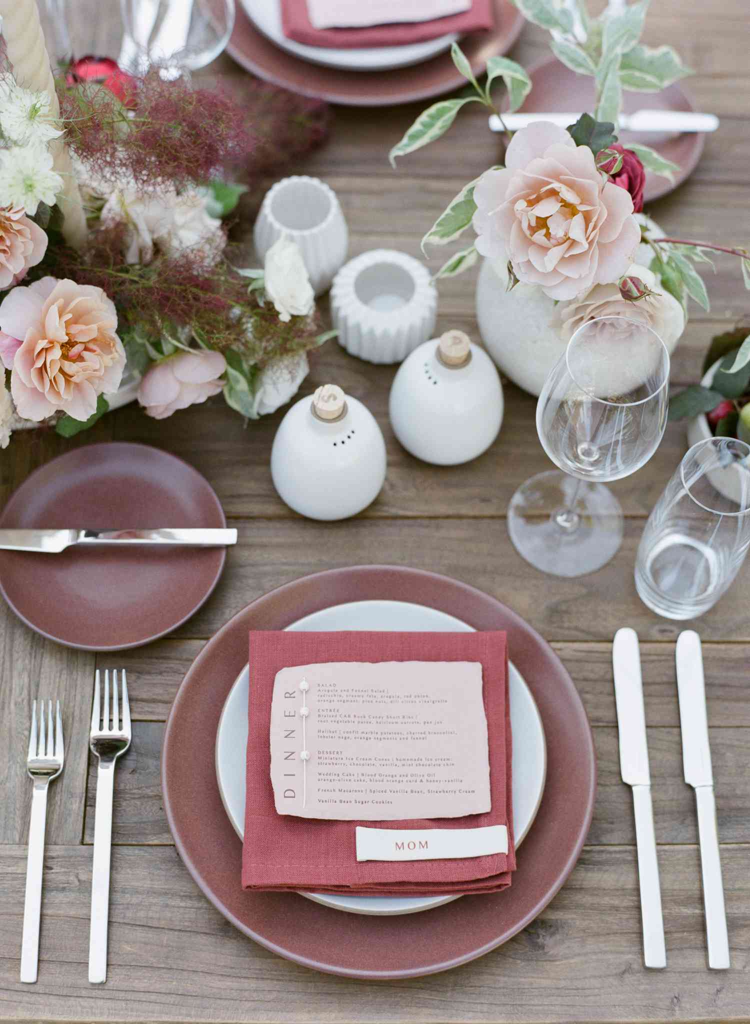 Wedding tablescape with wood able, burgundy plates, red napkins, pink menus, and pink florals