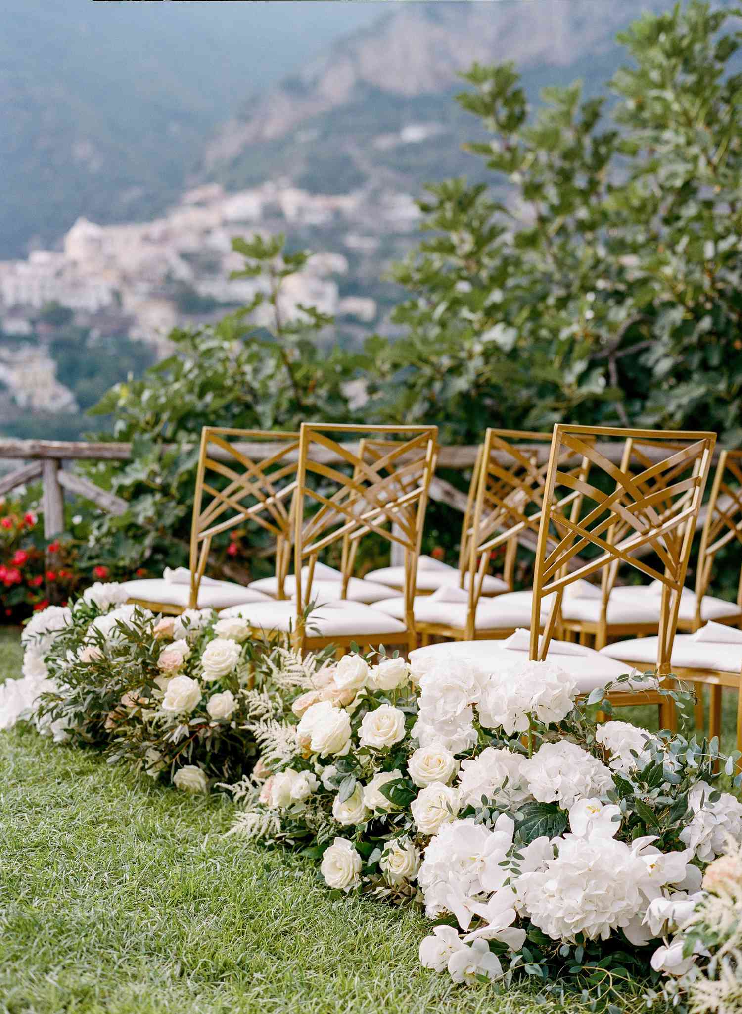 White hydranges and roses and ferns lining a grass aisle with Positano in background
