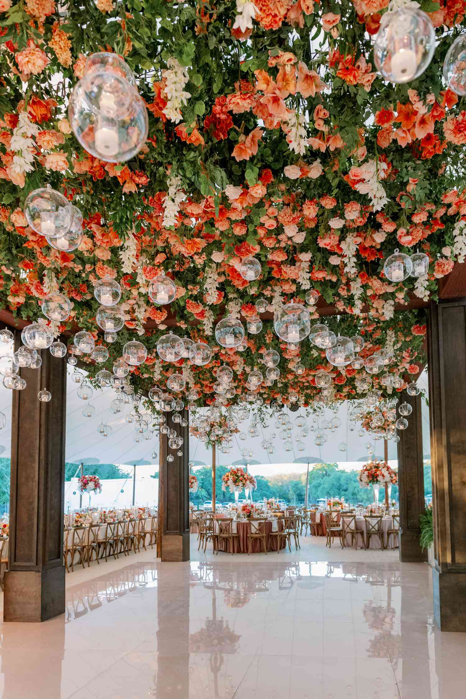 Dance floor hanging installation with peach and red flowers, greenery, and globe lights