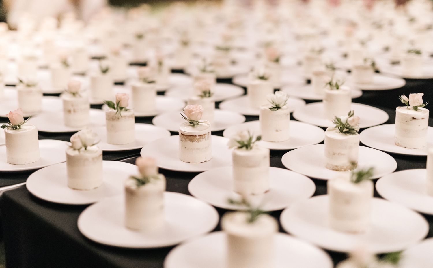 Individual white cakes on plates with single rosebuds on top