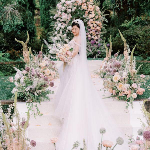 Brunette Bride Holding Pastel Bouquet in Front of Floral Arch and Floral Arrangements