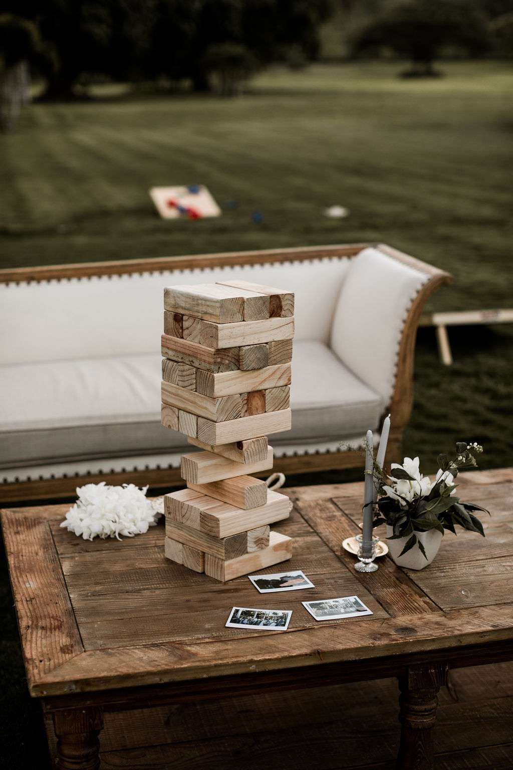 Giant Jenga sitting on a wooden table next to a white couch during an outdoor wedding reception.