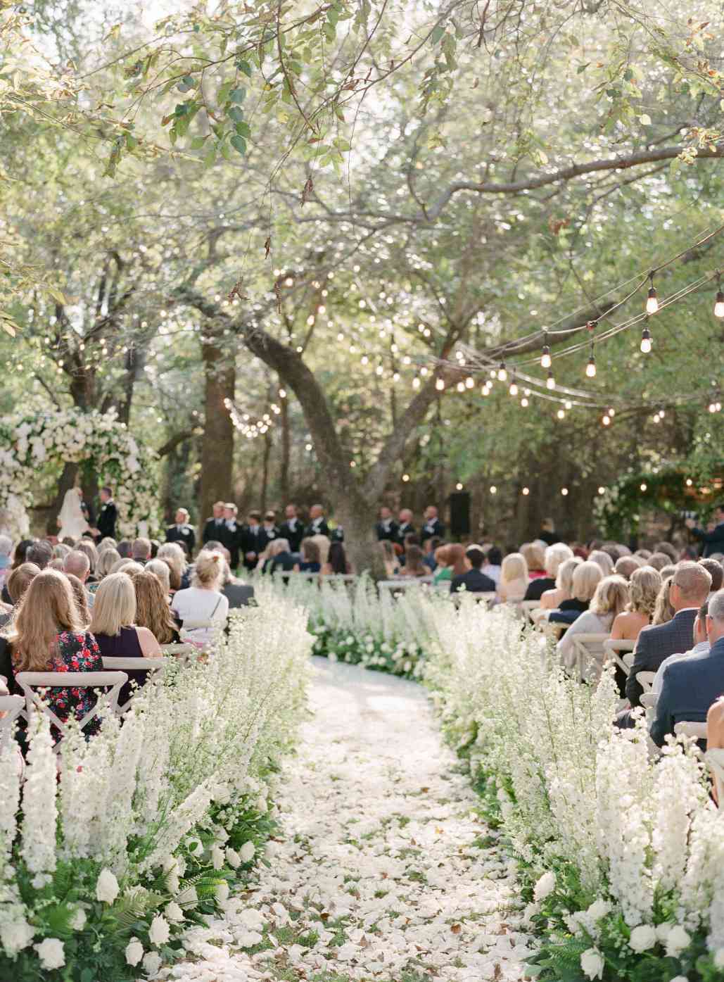 Flower and string-light lined aisle with people seated for wedding ceremony