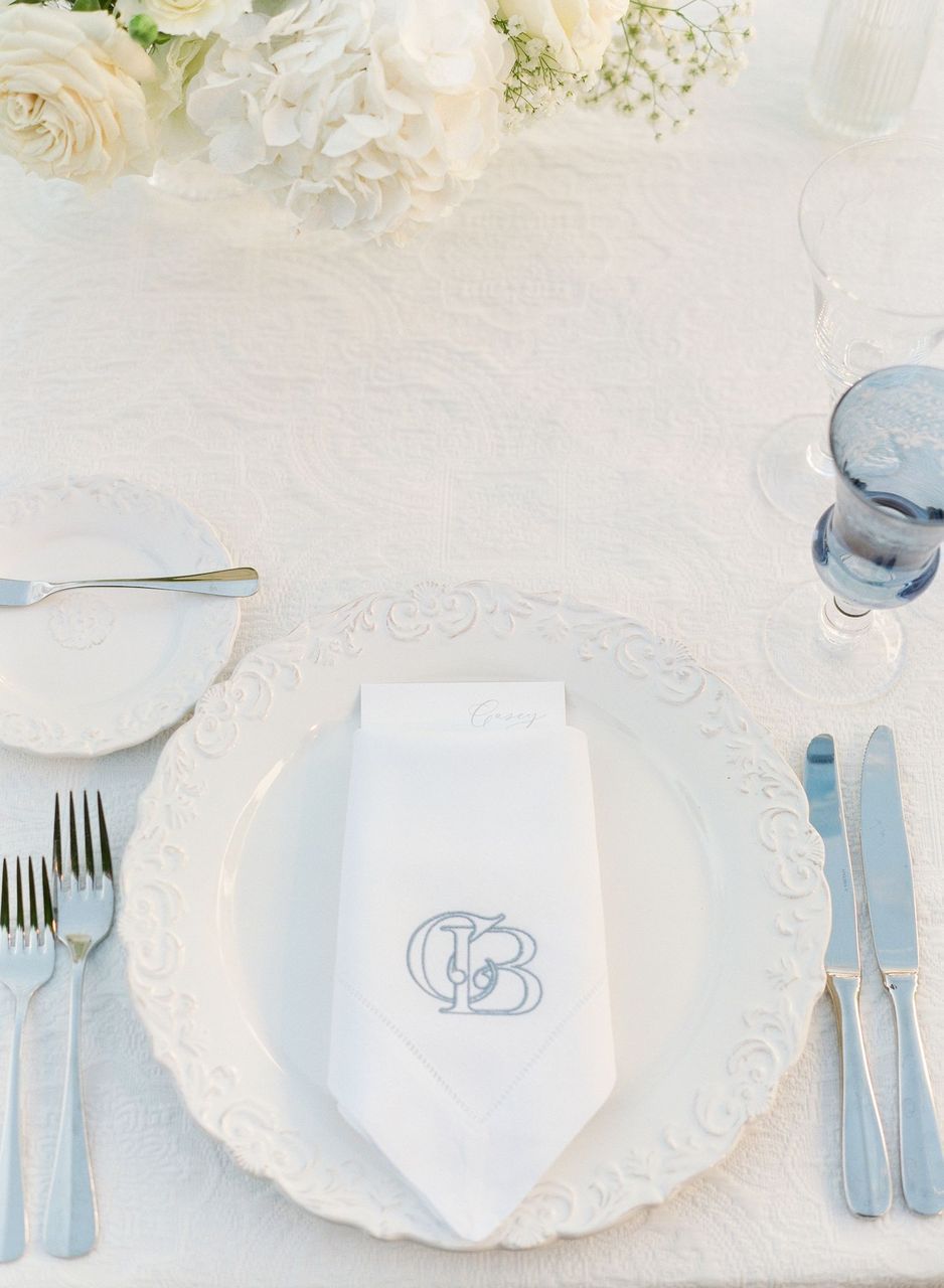 White tablescape with textured tablecloth, white plate, white napkin with monogram, and tinted glassware