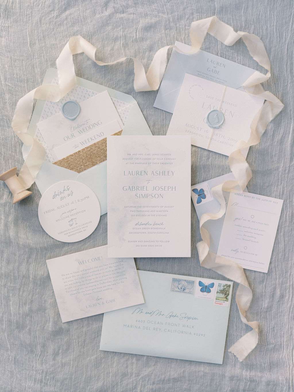 Light blue watercolor and white invitation suite with ribbon, butterfly stamps, and wax seal