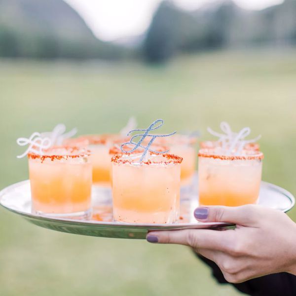 Peach-colored wedding cocktails served in rocks glasses on a silver tray at an outdoor reception.