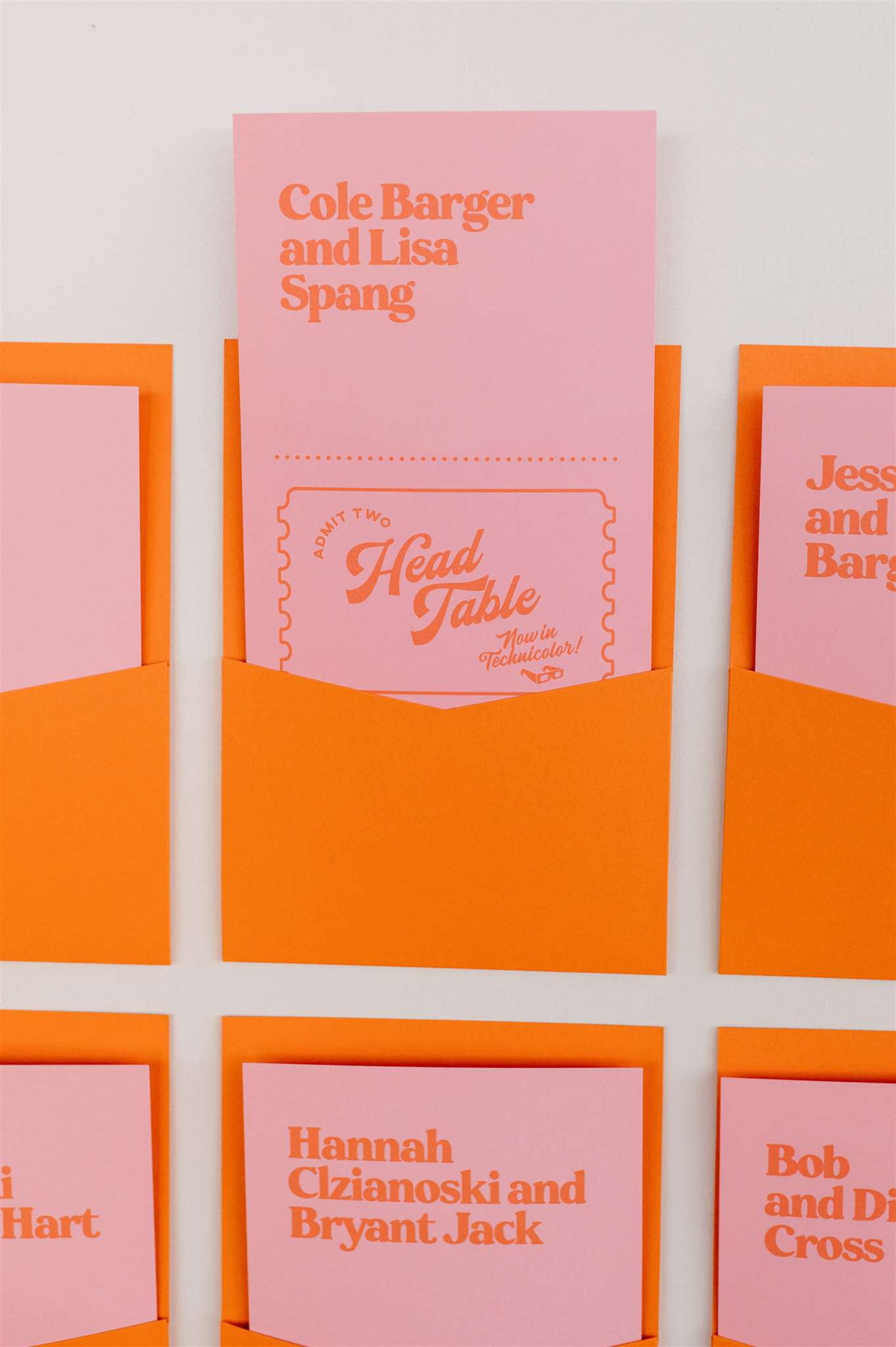 Escort card with names and ticket on pink paper in orange paper holder