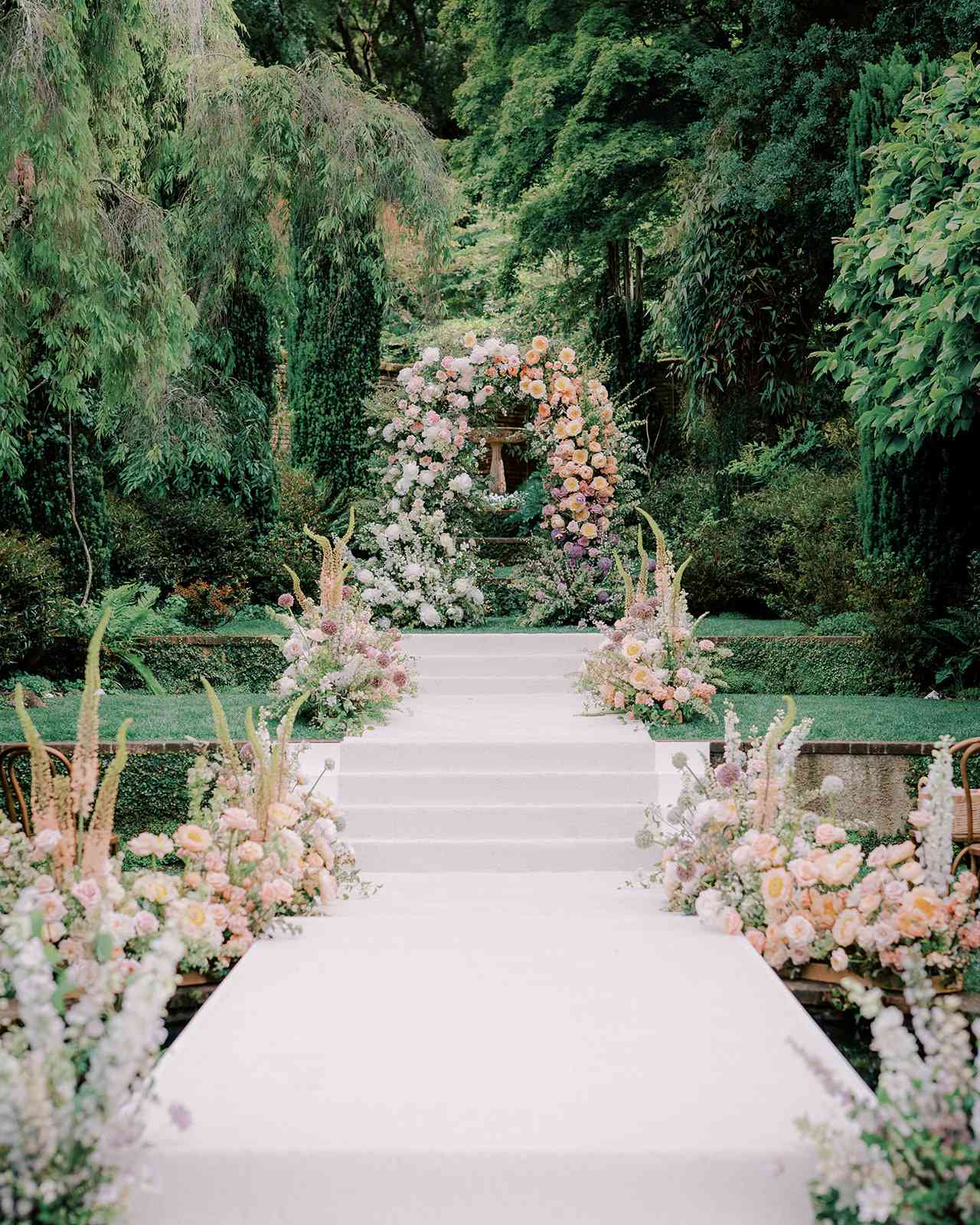 White aisle with stairs lined with pastel flowers in outdoor garden