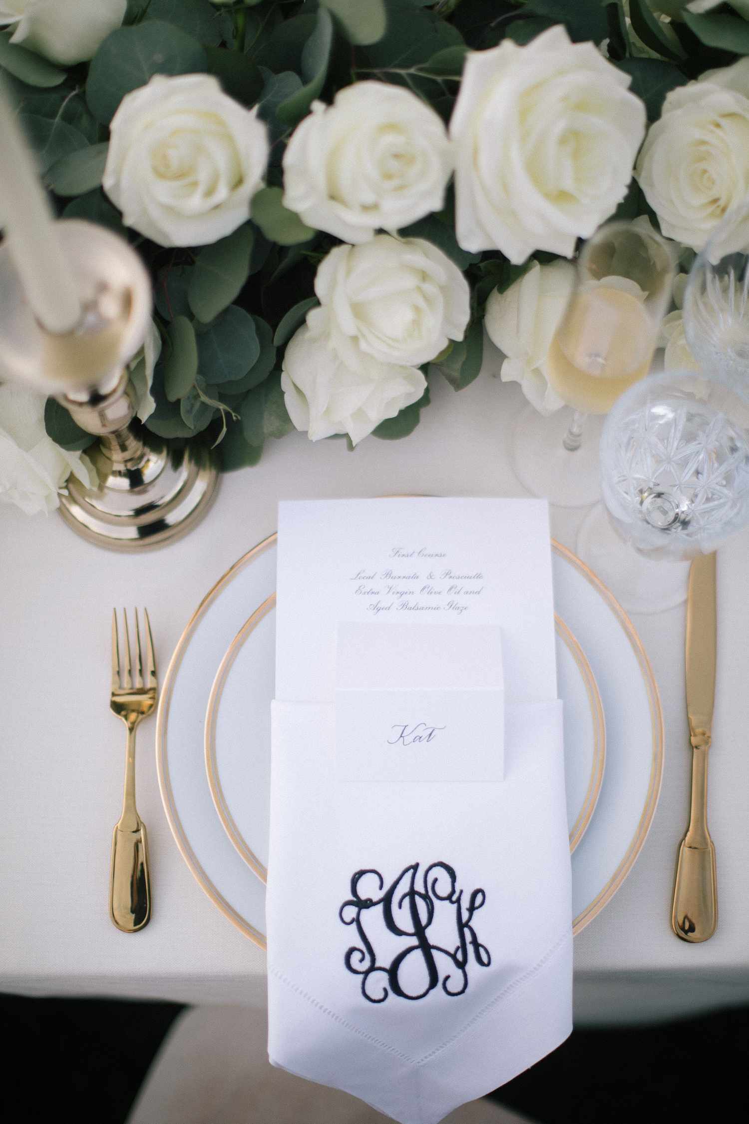 Wedding tablescape with monogrammed napkin, gold-rimmed plates, gold flatware, and white florals