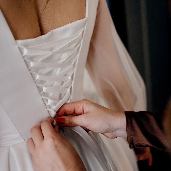 Maid of Honor Lacing Up Bride's Wedding Dress With Corset