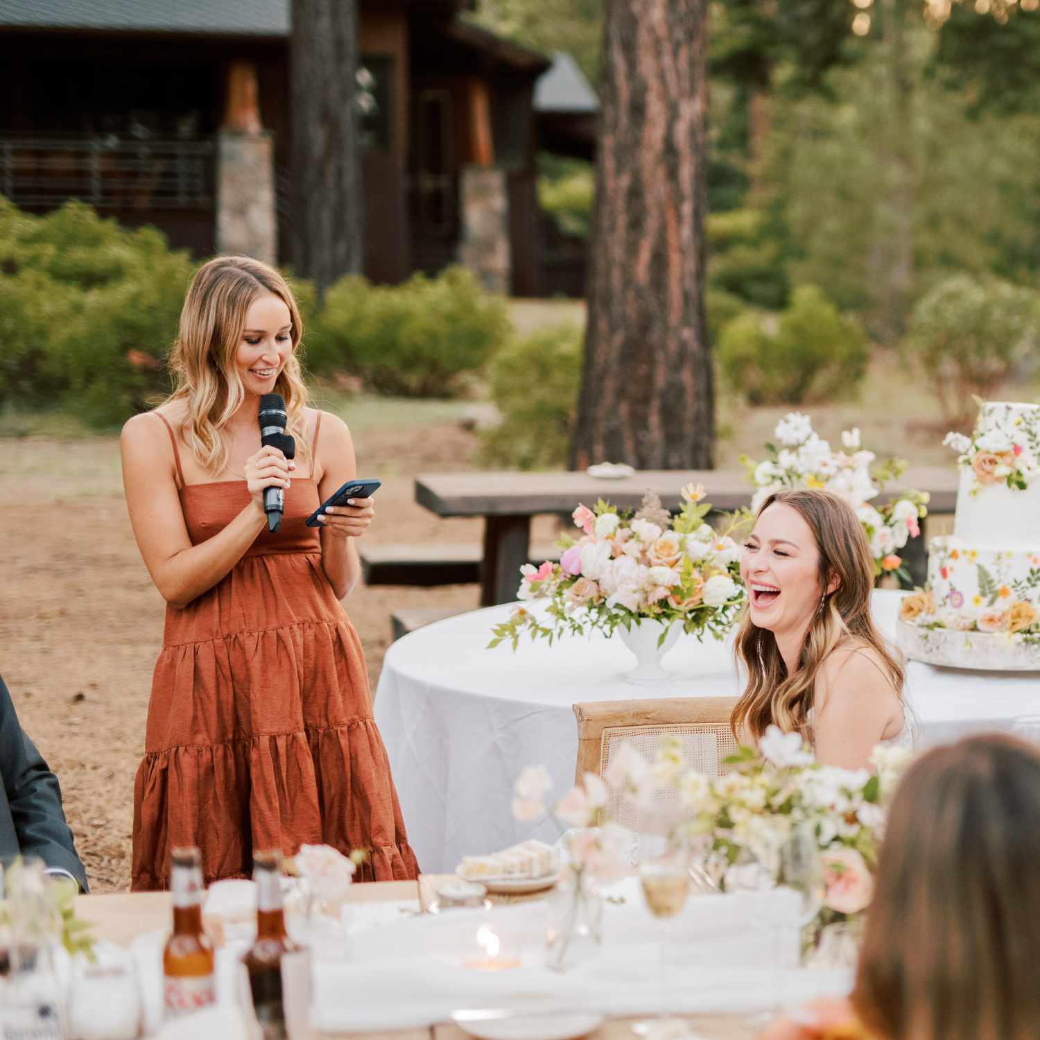 A maid of honor wearing an orange dress, giving a maid of honor speech at an outdoor wedding reception.