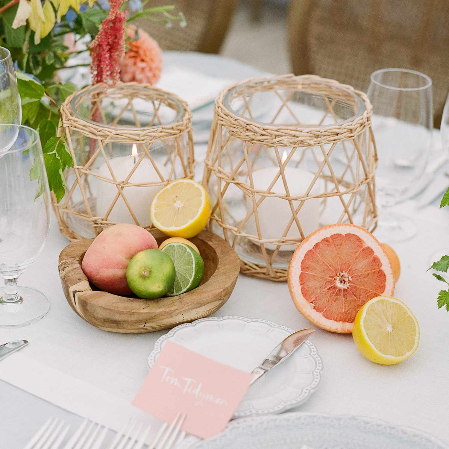 tablescape with citrusâgrapefruit, lemons, limes, and a peachâand white candles in a wicker-like vase